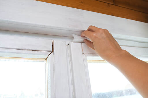Woman insulating old windows to prevent warmth heat leak and drafts in greenwich ct